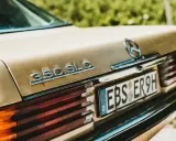 Detalle de un Mercedes 350 SLC dorado, con la luz de matrícula visible, listo para pasar la ITV.