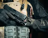 Dłoń w rękawiczce trzyma pistolet z zamontowanym na szynie taktycznym laserem do broni.