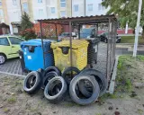 Kilka zużytych opon leży przed śmietnikami.