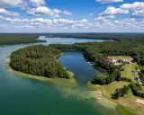 Malownicze jezioro Urszulewskie otoczone lasem, z hotelem i polem namiotowym na brzegu.