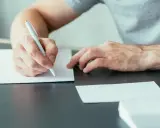 Mężczyzna pisze ręcznie list motywacyjny, przygotowując się do ważnego spotkania.