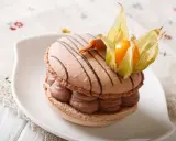 Un macaron chocolat au lait, garni de crème onctueuse et décoré d'une physalis, prêt à être dégusté.