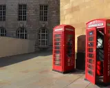 Klasyczne czerwone budki telefoniczne na brukowanym placu, w tle kamienna fasada budynku. Manchester miasto.