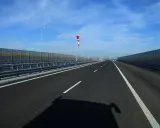 Pusta jezdnia nowej drogi z barierami dźwiękochłonnymi i wiatrowskazem.