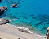 Spiaggia dorata e mare cristallino con scogli a Capo Cozzo.