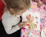Dziewczynka maluje złotą farbą gipsową figurkę renifera.