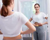 Mujer se mide la cintura con cinta métrica, sonriendo al verse en el espejo. No hay evidencia de que el diu de cobre engorde.
