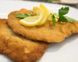 Zwei goldbraune Schnitzel, perfekt in Butter gebraten, garniert mit Zitronenspalten und Petersilie auf einem weißen Teller.