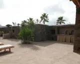 Un cortile in cemento trasformato con piante rigogliose, un barbecue in pietra e comodi lettini. Idee per come abbellire un cortile in cemento.