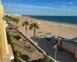 La **playa de la Costilla** con palmeras y gente disfrutando del sol. El mar azul se extiende hasta el horizonte.