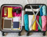 Packar för resan! I det öppna incheckat bagage sas ligger kläder, kamera, solkräm, glasögon, surfplatta och pass.