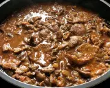 Fricandó de ternera cocinándose en una sartén, con trozos de carne tierna en una salsa espesa y aromática.