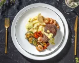 Ein köstliches Surf and Turf Rezept: saftiges Steak, Garnelen, Kartoffelpüree und gegrilltes Gemüse auf einem Teller.