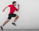Ein Mann in rotem Shirt und schwarzen Shorts läuft mit hoher Kadenz gegen eine Betonwand.