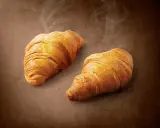Dwa złociste, parujące croissanty na brązowym tle. Pyszne, choć warto pamiętać o ich kaloryczności.