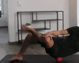 Mann dehnt den Piriformis mit einem roten Ball unter der Hüfte.