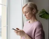 Besorgte Frau blickt auf ihr Handy. Sie fragt sich, ob ihr Handy ausspioniert wird.