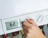 Dłoń reguluje ustawienie pieca gazowego. Na wyświetlaczu 62.1°C, obok manometr i pokrętła regulacji.