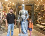 Un padre y su hija posan junto a una armadura de caballero en una tienda de souvenirs en Toledo con niños.
