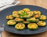Rondes et grillées, ces courgettes au four sont présentées sur une assiette grise, garnies d'une touche de verdure. Un délice simple et savoureux.