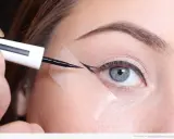 Aplicando delineador con cinta para aprender como hacer la raya del ojo para principiantes. Ojo azul, ceja definida, delineador negro.