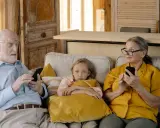 Abuela paterna celosa mira con recelo mientras el abuelo y la nieta están absortos en sus teléfonos.
