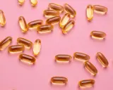 Capsule dorate sparse su sfondo rosa, utili per la vitamina D in gravidanza.