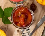 Tarro de compota de melocotón casera, con melocotones frescos y hojas verdes alrededor.