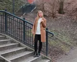 Kobieta w płaszczu i swetrze prezentuje basicowe stylizacje na tle schodów i parku.