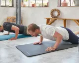 Dwóch mężczyzn wykonuje ćwiczenia na triceps w domu, robiąc pompki na matach.