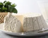 Un morceau de ricotta fraîche sur une assiette, avec des herbes en arrière-plan. Idéal pour connaître les calories de la ricotta.