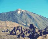 Vulkan Pico del Teide mit felsiger Landschaft im Vordergrund und blauem Himmel.