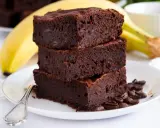 Stos puszystych brownie z bananami, ozdobiony ziarnami kawy, na talerzu z bananem w tle.