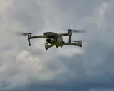 Eine graue Drohne mit roten Lichtern fliegt im bewölkten Himmel. Man kann die Propeller sehen, die sich drehen, während die Drohne in der Luft schwebt. Es ist ein tolles Gefühl, eine Drohne fliegen zu lassen.