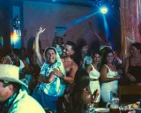 Gente celebrando y bailando en una fiesta, con luces de discoteca y un ambiente festivo. Parece una despedida de soltero con juegos y mucha alegría.