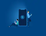 Dos personas usan sus móviles junto a un gran smartphone. Explica qué es Bizum y cómo funciona, una forma fácil de enviar dinero.