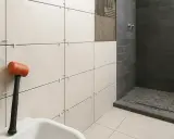 Herramientas para alicatar suelo de baño. Mazo de goma naranja junto a azulejos blancos y grises en proceso de instalación.