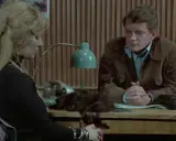 Kobieta z blond włosami i mężczyzna siedzą przy biurku. Na biurku leży peruka. Czy to sprawa dla "07 zgłoś się"?
