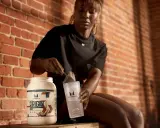 Frau bereitet einen proteinshake mit milch oder wasser vor. Sie schöpft Pulver aus einem Behälter in einen Shaker.