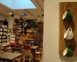 Mysig cafe inredning med bokhyllor, bord och stolar. Tre muggar hänger på en träplatta.