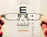 Okulary poprawiające wzrok, przez które widać tablicę Snellena z literą "E" i cyfrą "2".