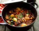 En mustig boeuf bourguignon i gjutjärnsgryta med champinjoner, lök och örter.
