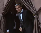 George Clooney, dapper in a tuxedo, emerges from behind velvet curtains. A perfect tix vs suit moment.