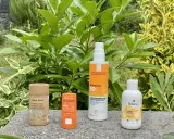 Quatre produits de protection solaire, dont un écran solaire physique, sont alignés sur un muret, entourés de verdure luxuriante.