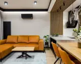 Nowoczesny salon bez sufitu z pomarańczową kanapą, drewnianym stołem i designerskimi lampami.