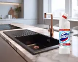 Domestos na zatkany zlew. Nowoczesna kuchnia z czarnym zlewem i złotą baterią, obok butelka Domestos.