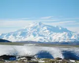 Pokryty śniegiem najwyższy masyw Wielkiego Kaukazu, Elbrus, góruje nad ośnieżonymi wzgórzami i zielonymi dolinami.