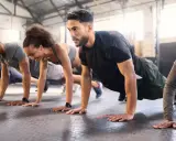 Gruppe trainiert Liegestütze im Fitnessstudio. Ein Mann mit Bart konzentriert sich auf sein ganzheitliches Training.