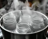 Fünf leere Glasflaschen werden in einem Topf mit kochendem Wasser sterilisiert, um sie für die Konservierung vorzubereiten.