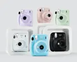 Pięć aparatów Instax Mini 11 w różnych kolorach: fioletowym, różowym, zielonym, białym, niebieskim i czarnym.